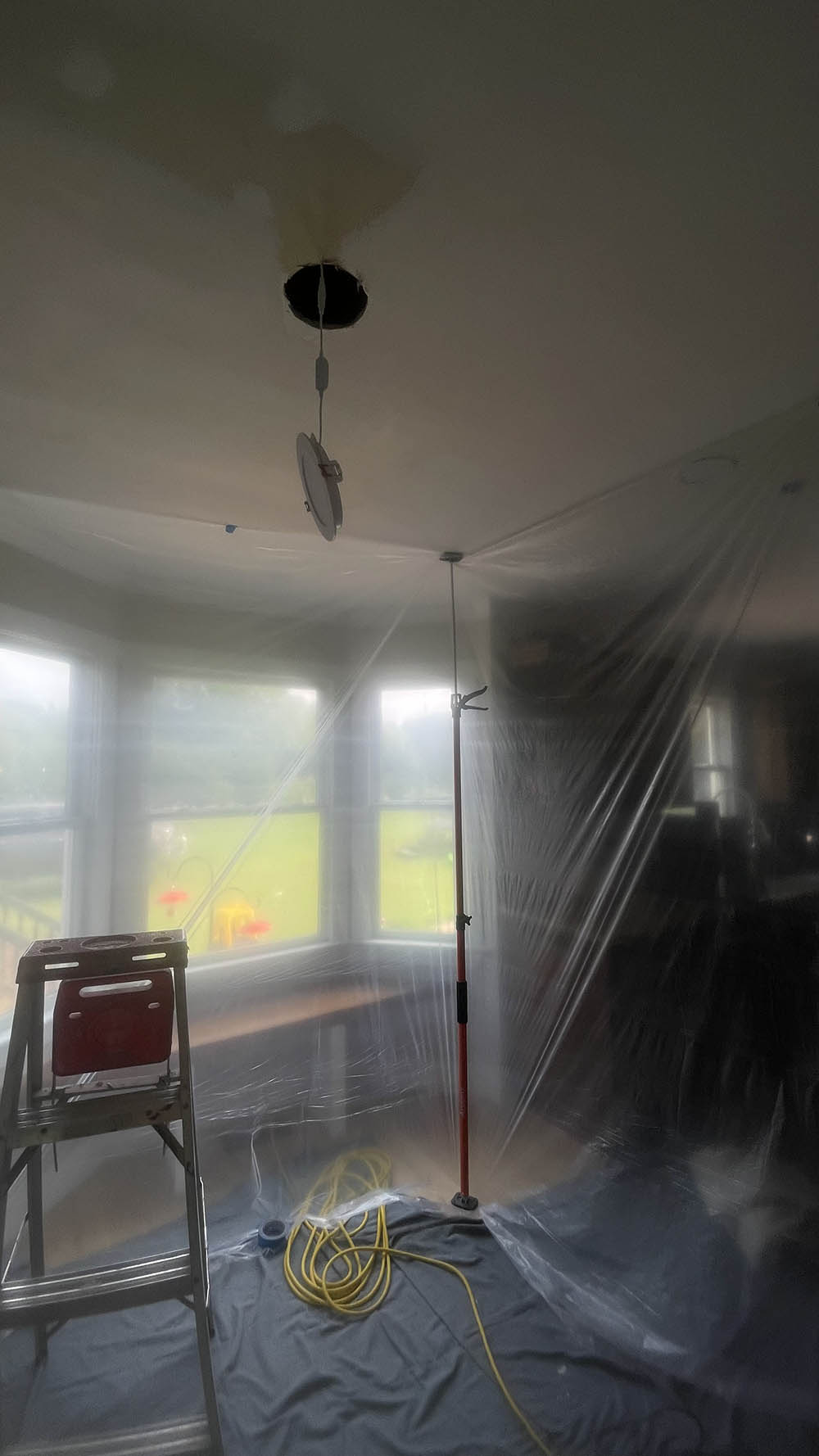 Tension poles securing clear plastic sheeting around kitchen bay window